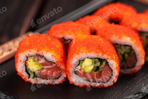 Preview: Close up California sushi roll with salmon avocado, cucumber and tobiko caviar served on black board