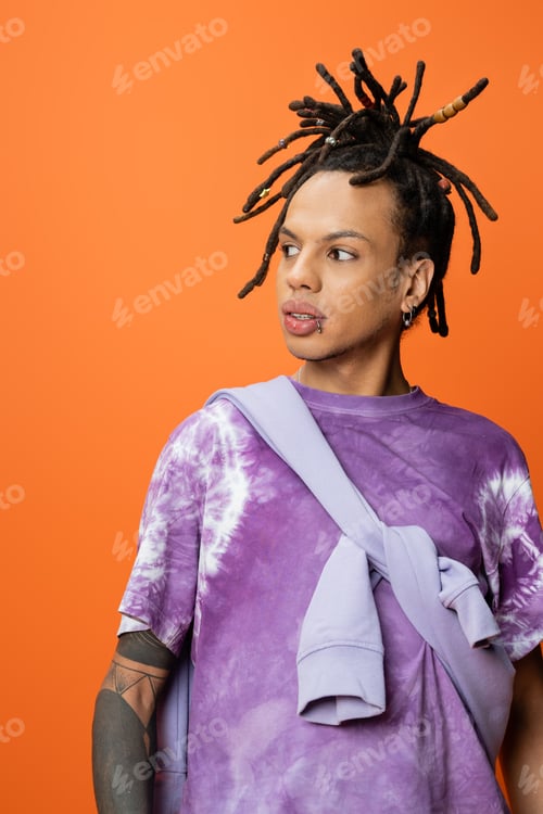 Preview: stylish multiracial man in tie-dye t-shirt looking away isolated on orange