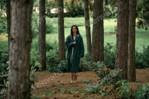 Preview: Stylish young woman exploring a lush green forest in a trendy raincoat