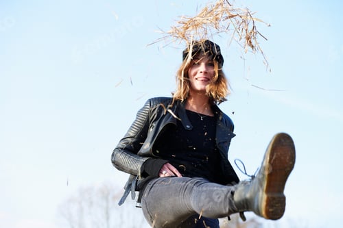 Preview: Woman in cap kicking up straw against blue sky