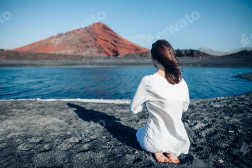 Preview: Back view of woman in white clothes praying in black sand beach
