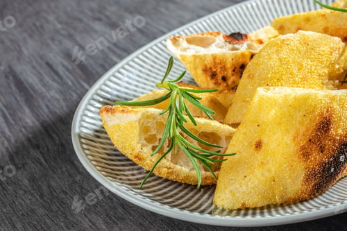 Preview: crispy focaccia bread slices with rosemary on a plate close up. top view