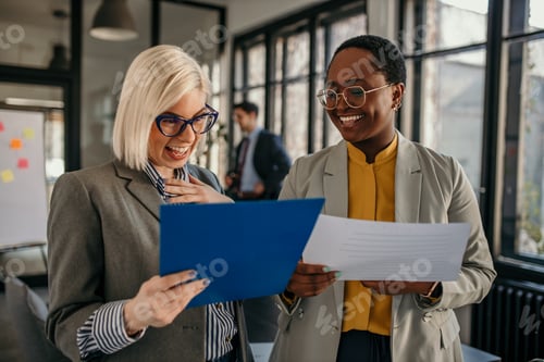 Preview: Businesswomen sharing positive news while reading documents in office