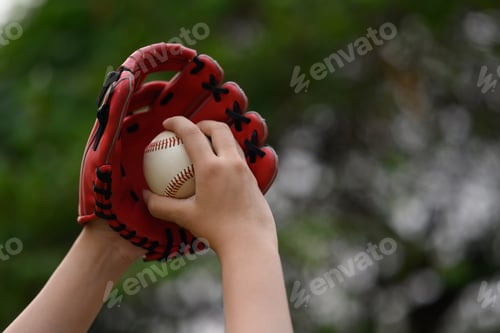 Preview: Hand of baseball player in a leather glove holding ball on blurred green background