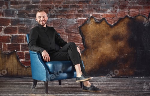 Preview: A young man in an armchair in a loft room is looking at the camera. Facing difficulties, not afraid