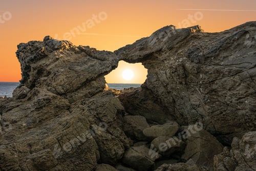 Preview: Ocean Sun Shining Through Rock Formation at Sunset