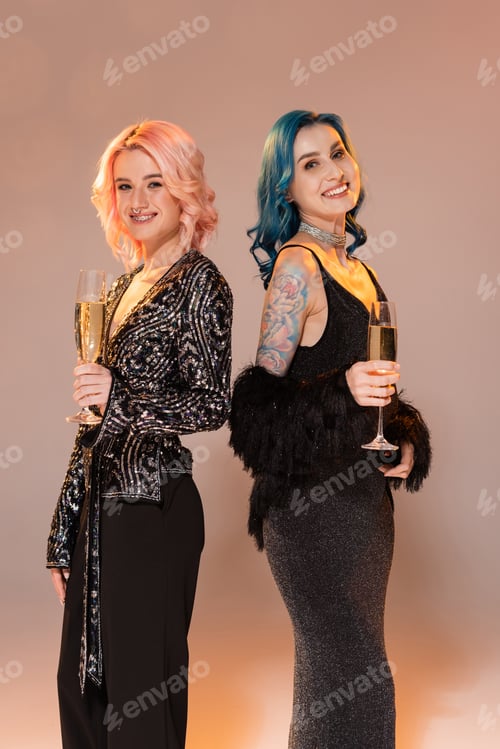 Preview: queer friends in festive elegant clothes holding champagne and smiling at camera on beige background