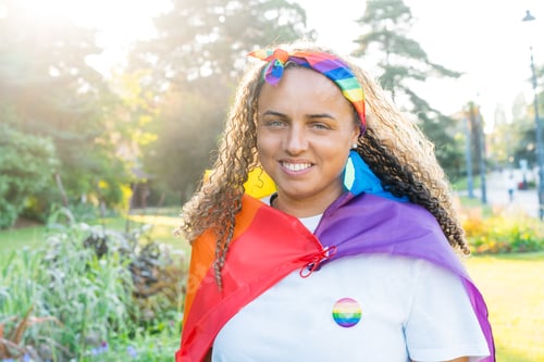 Preview: Smiling mixed-race woman wrapped in a rainbow flag. A young lesbian activist