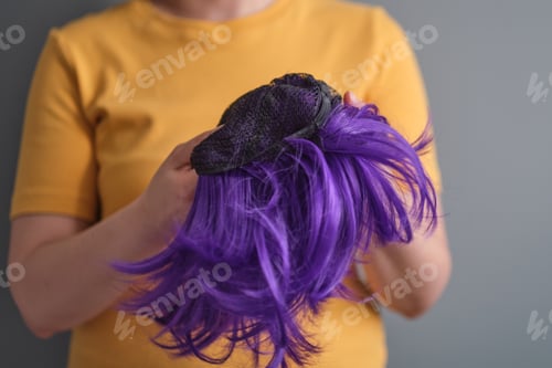 Preview: woman holds a bright purple wig in her hands. Womens beauty concept