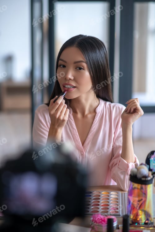 Preview: Dark-eyed woman using lipstick while finishing makeup