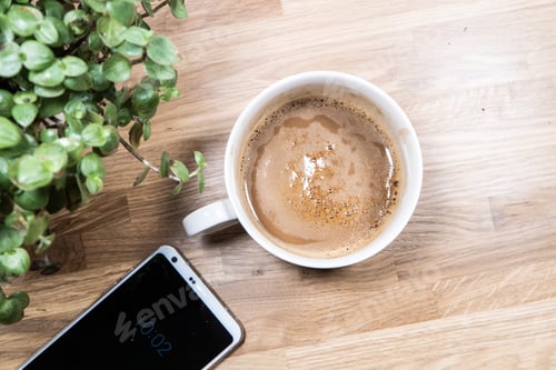 Preview: Flat lay shot of a cup of coffee, a smartphone and a houseplant on a wooden table