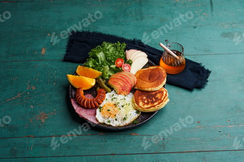 Preview: Breakfast pancakes, fried eggs, sausages, ham and fruit.