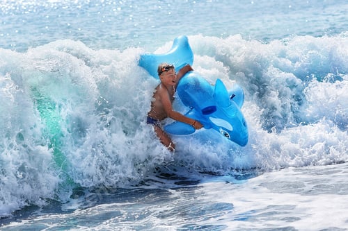 Preview: a boy and an inflatable dolphin in a big wave of the sea