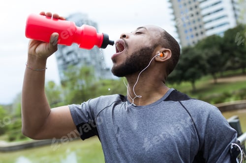 Preview: Fit and sporty young man drinking water in the city.