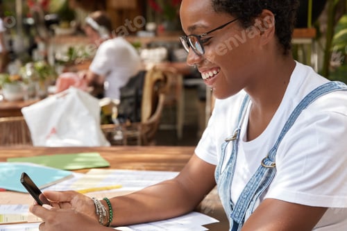 Preview: Sideways shot of cheerful hipster girl dressed in casual white t shirt, checks email box on smart ph