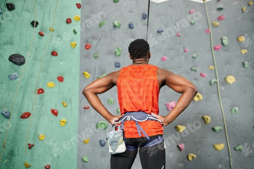 Preview: back view of sporty african american man ready to climb up bouldering wall with his hands on hips