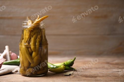 Preview: Glass jar with pickled peppers on wooden table. Space for text