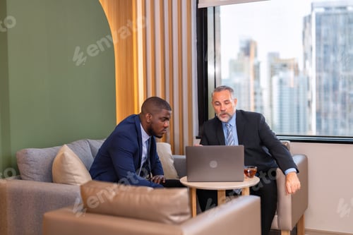 Preview: Two businessmen sitting on sofa working discuss on financial forecast together on laptop information