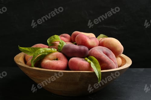Preview: Fresh ripe donut peaches with leaves in bowl on dark table