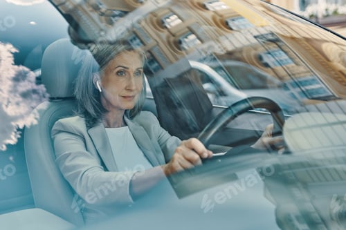 Preview: Mature beautiful woman in smart casual wear looking ahead while driving car
