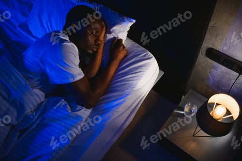 Preview: Serene calm handsome young black man sleeping well alone on orthopedic soft pillow under warm duvet