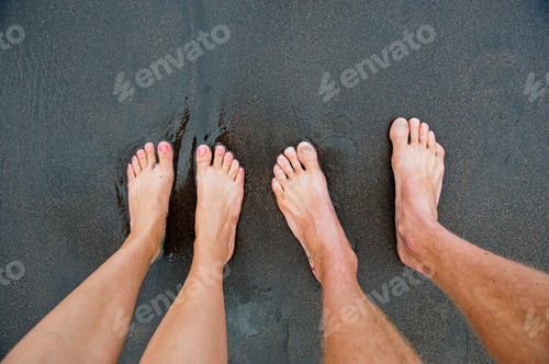 Preview: Two people standing barefoot on a sandy beach, viewed from above.