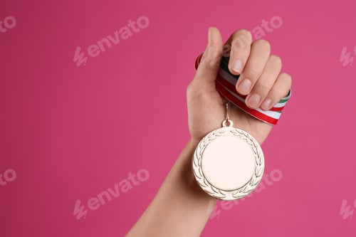 Preview: Woman holding golden medal on pink background, closeup. Space for design