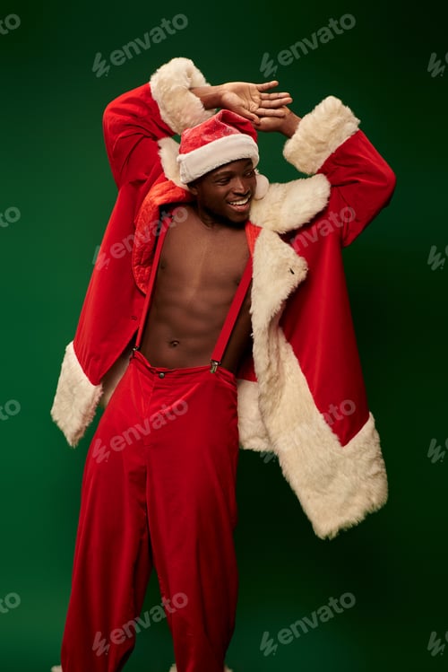 Preview: hot african american guy in christmas costume on shirtless body smiling and looking away on green