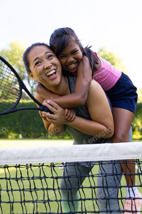 Preview: Outdoors biracial mother and daughter smiling with tennis rackets on court