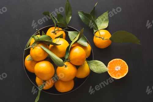 Preview: Fresh mandarins with leaves in bowl on black. Healthy eating concept.