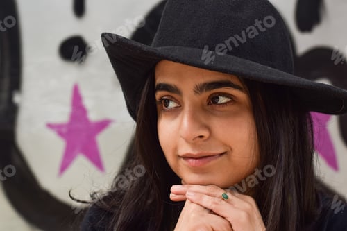 Preview: Closeup portrait of young stylish teenage girl in fedora hat in front of graffiti wall