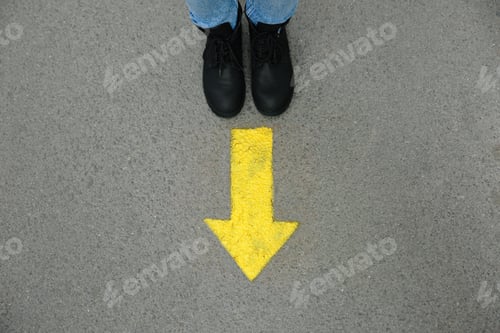 Preview: Person standing near arrow on asphalt, top view