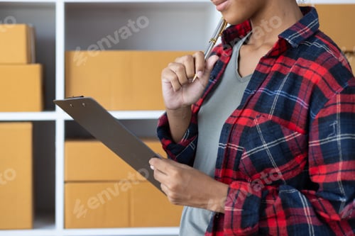 Preview: Young African woman starting an online shopping business from home is preparing package.