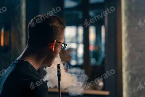 Preview: A man in glasses smokes traditional hookah pipe A man exhales thick smoke in a hookah cafe