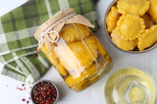 Preview: Pickled pattypan squashes in jar, bowl, oil and peppercorns on white tiled table, flat lay