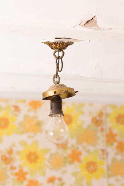 Preview: broken old bulb hanging from peeling ceiling, floral wallpaper out of focus