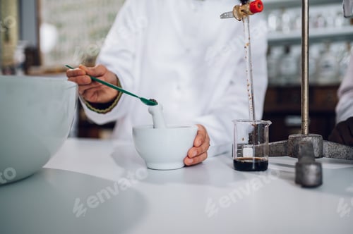 Preview: Close up of a pharmacist adding an ingredient to a mortar while making a drug in a vintage drugstore