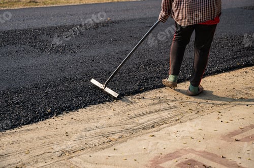 Preview: Construction worker using tool spread the hot-mix asphalt road accurately level covering on highway