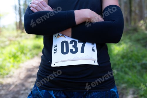 Preview: Unrecognizable female trail athlete posing with race number