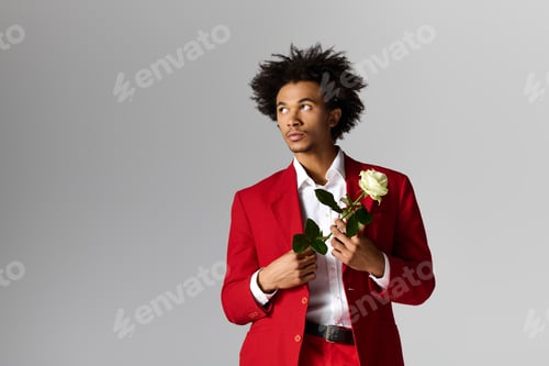 Preview: Young man exudes charm in elegant red attire with a fresh rose in hand