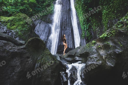 Preview: Woman enjoying near hidden in jungle cascade waterfall in Bali. Slim body and black swimsuit