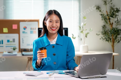 Preview: Happy entrepreneur working on computer and drinking coffee in her office