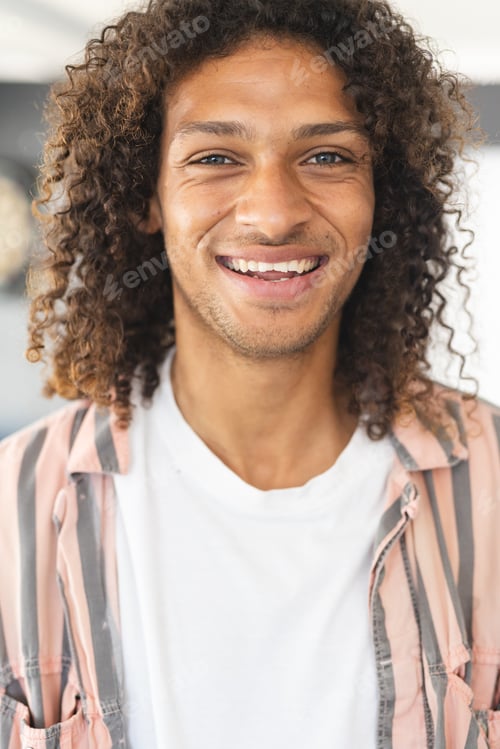 Preview: Young biracial man with curly brown hair smiles warmly