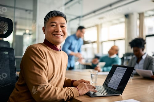 Preview: Happy Asian businessman working on laptop during a meeting in the office and looking at camera.