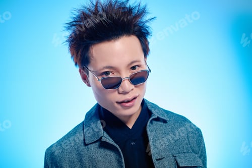 Preview: Stylish young man with trendy hairstyle posing confidently against a vibrant blue background