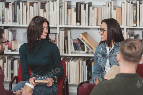 Preview: smiling girls sitting in library and looking at each other