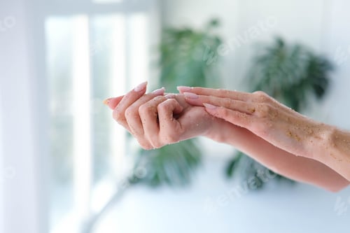 Preview: Close-up woman is hands with coffee massage scrub on monstera blurred background.