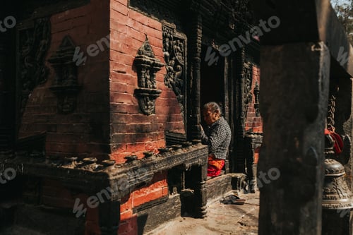Preview: Nepali woman sitting in a red brick with wooden sculptures building in Pashupatinath Hindu Temple