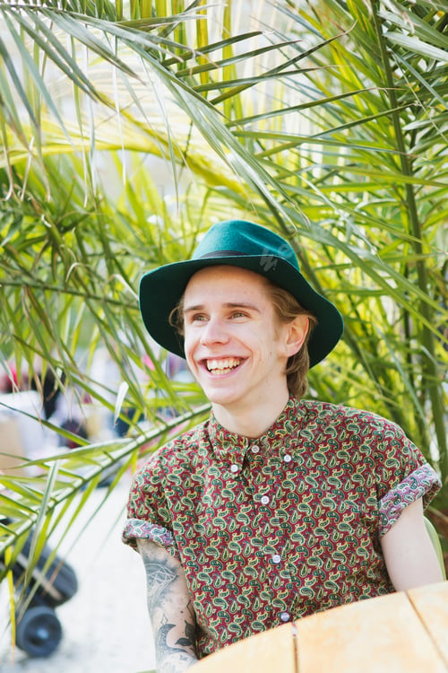 Preview: Smiling young man sitting at cafe against plant