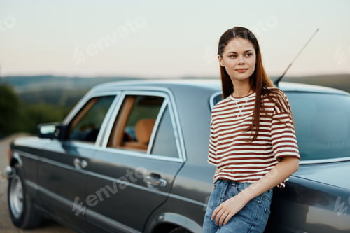 Preview: A woman driver near her retro car relaxing from the tough road and enjoying the scenery